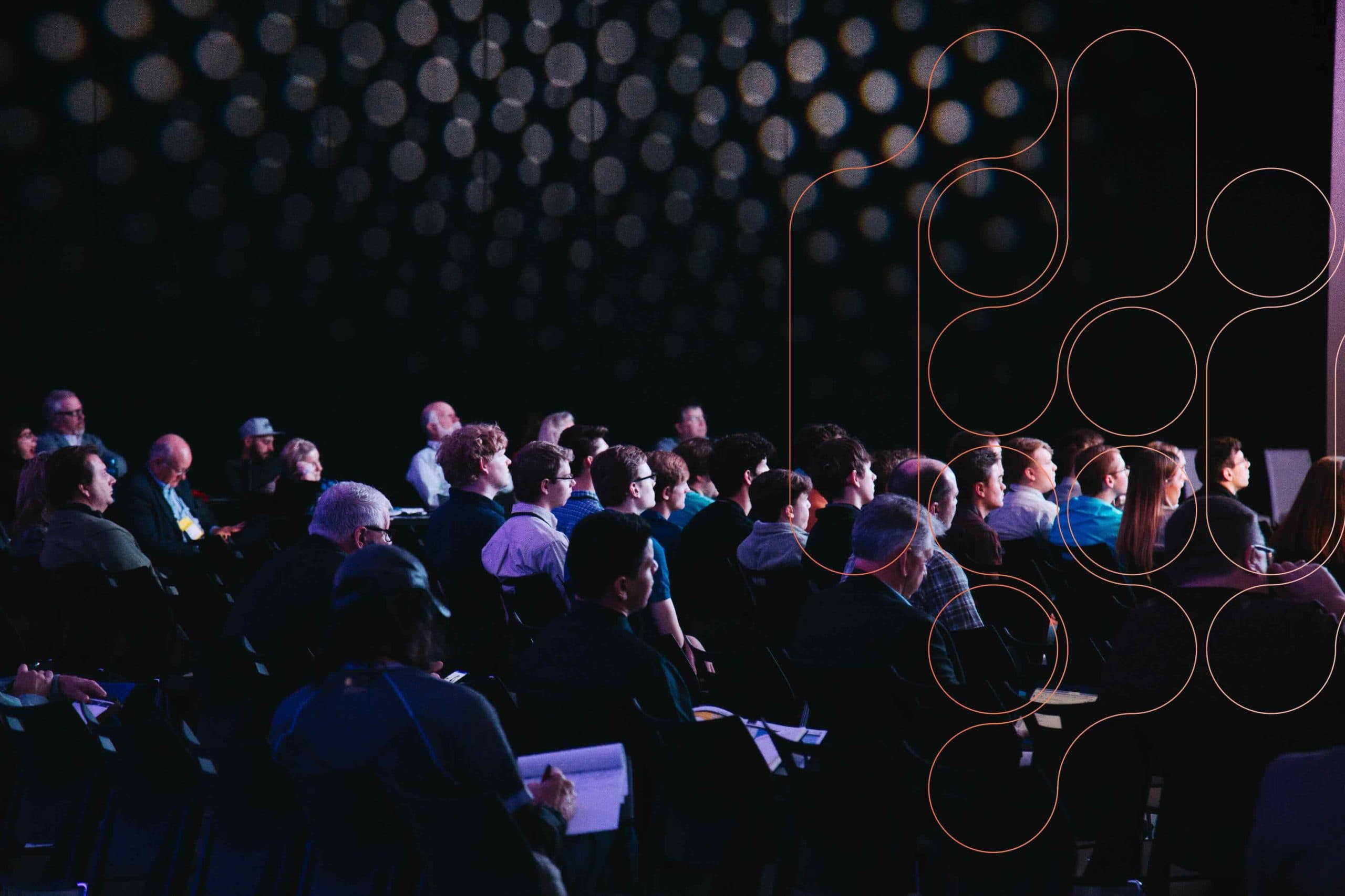 A photograph of an audience in a dark room.